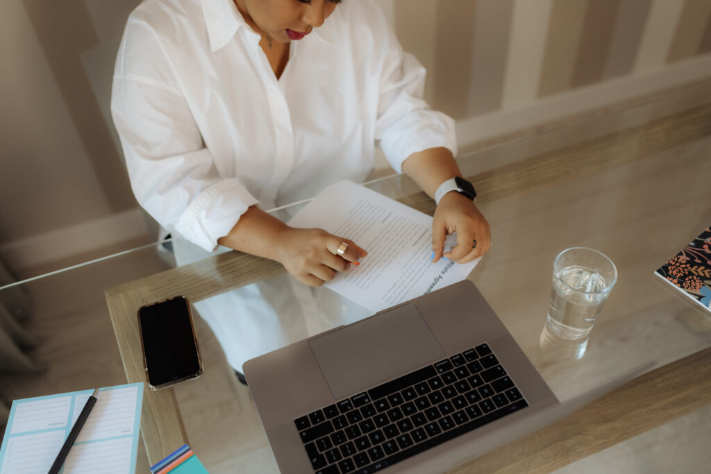 A wedding creative studying Pinterest metrics on her laptop while making planning notes in a leather notebook beside her coffee